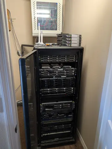 Oct 2026. The big rack today. Most of it is retired; the 12-bay R730xd at the top still runs TrueNAS for the cluster. The two white antennas on top are Nabu Casa Z-Wave and Zigbee radios.